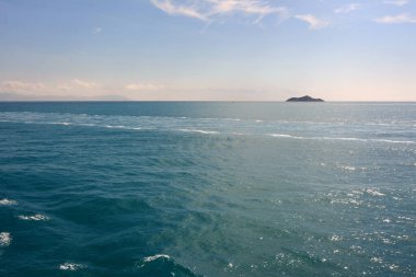 Turkuaz, parlak yaz güneşinin altında ufka doğru sakin bir deniz ve uzakta küçük bir ada.