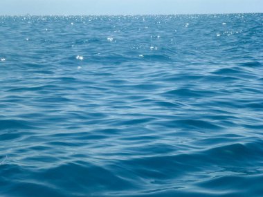 Deniz dalgalarının sakin yüzeyi parlak güneşin altında ufukta dalgalanır. Yaz deniz manzarası