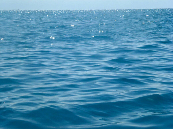 The calm surface of the sea waves under the bright sun to the horizon. Summer seascape