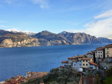 Resimli bir İtalyan sahilindeki eski evlerin kiremitli çatıları. Arka planda deniz körfezi ve dağlar var. Yaz turist manzarası