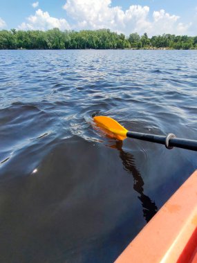 Nehrin sularındaki bir teknenin turuncu plastik küreği suyu kepçeler. Arka plandaki uzak kıyı. Yaz sporları ve eğlence