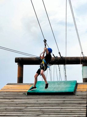 Spor teçhizatlı genç bir çocuk lunaparkta teleferiğe binmeye hazırlanıyor. Aşağıdan gökyüzünün arkaplanından görüntüle