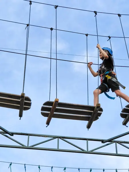 stock image A teenage boy in a safety harness crosses a suspension bridge on a wooden obstacle course in an amusement park. Summer sports