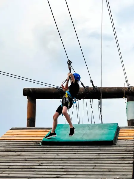 stock image A teenage boy in a sports safety gear prepares to go down a cable car in an amusement park. View from below on the background of the sky