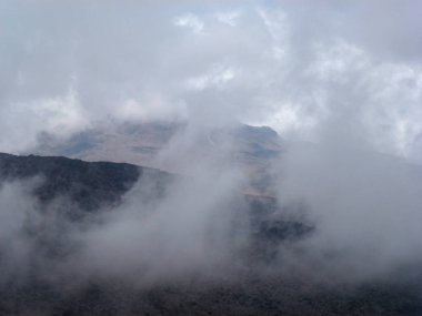 View of the slope of a large mountain covered with a white cloud against the background of the sky. Beautiful summer landscape for climbing and hiking clipart