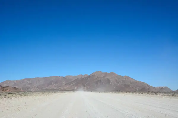 stock image A wide dirt road in perspective in the desert leads to distant mountains under a clear blue sky