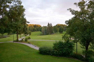 Golf sahasının manzarası. Ağaçların arasında güzel bir çim ve patika var. Boş zaman ve açık hava sporları. Yaz doğal manzarası