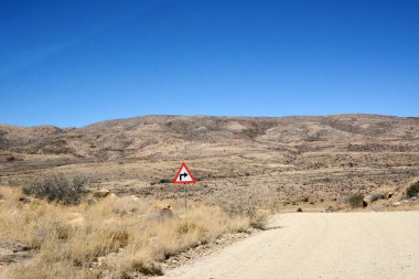 Çöldeki toprak yolun kenarında açık mavi bir gökyüzünün altında bir dönüş işareti var. Ulaşım ve doğa