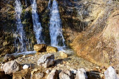 Gölgede, küçük bir şelalenin birkaç akıntısı dik dağ kayalarından aşağı akar. Doğa manzarası. Uzun pozlama