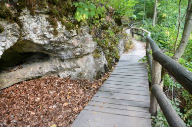 Sonbahar ormanındaki bir mağaranın yanında, perspektifi parmaklıklı, ahşap bir patika. Doğa yürüyüşü. Turist doğası