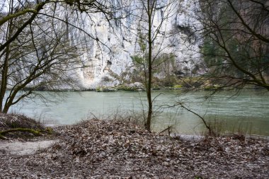 Sakin bir sonbahar nehri yüksek kayaların altında akar. Ön planda bir yığın kuru park yaprağı var. Sonbahar kasvetli manzarası