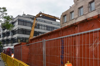 Şehirde geçici çitleri ve inşaat enkazı için konteynırları olan bir inşaat alanı. Kazıcının bir kısmı görünür.