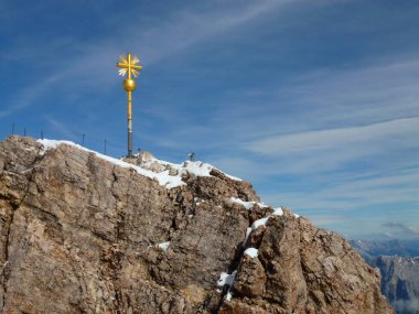Mavi gökyüzünün arka planına karşı dağa demirden sarı bir haç monte edilmiş. Almanya, Bavyera 'da dağ zirvesi.