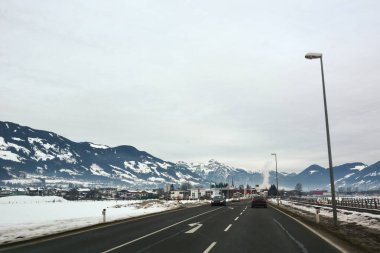 A perspective view of a winter asphalt road against the background of mountains. Winter trip or vacation. Cars are driving on the road clipart