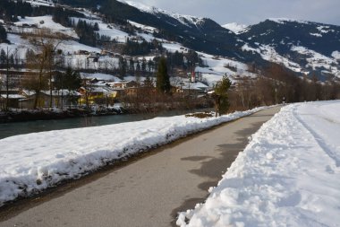 Kış nehrinin kenarındaki perspektif içinde yürüme ve arka plandaki karlı dağları tefekkür etme yolu. Dağlara yakın küçük bir köy..