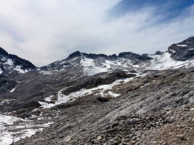 Kayalık kayalık dağ yamaçları kısmen karla kaplı. Onların üzerinde beyaz bulutlu bir gökyüzü var. Kış manzarası ve vahşi yaşam.