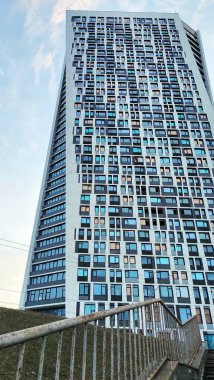 Mavi gökyüzüne karşı fütürist şekilli bir gökdelen. Modern mimarinin bir örneği. Birçok pencere bir şablon içinde tekrarlanır. Alt görünüm