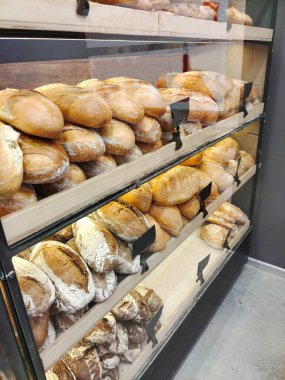 Fırının perspektifindeki raflarda çeşitli şekillerde ve kompozisyonlarda lezzetli taze ekmek. Çeşit çeşit ekmeği olan modern fırın.