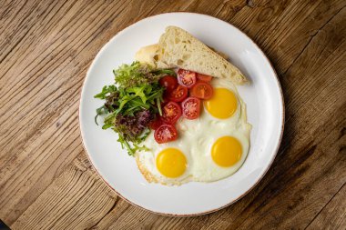 a delicious breakfast on a plate prepared in the restaurant. Fried eggs with tomatoes and salad