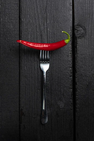 stock image A red chili pepper on a fork on a black table.