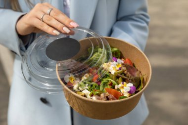 Bir kadın elinde bir kutu salata tutuyor..