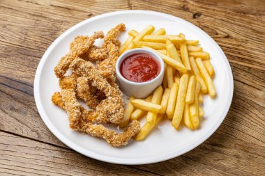 Tahta bir masada patates kızartması ve ketçaplı tavuk nugget tabağı..