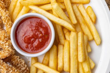 Tahta bir masada patates kızartması ve ketçaplı tavuk nugget tabağı..