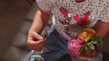 Bir kız bir kafedeki cam bardaktan dondurma yiyor. Yakın plan.