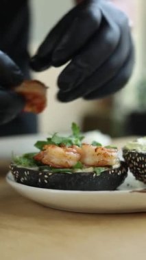  Siyah eldivenli şef karidesli bir hamburger hazırlar.