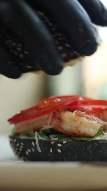  Siyah eldivenli şef karidesli bir hamburger hazırlar.