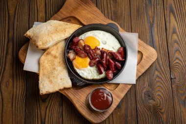 Tahta bir masada, tavada yumurta ve sosisle nefis bir kahvaltı.