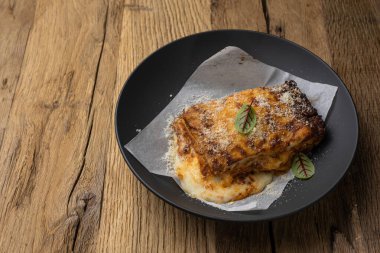 Tahta bir masada siyah tabakta bolonez lazanyası. Kapat.