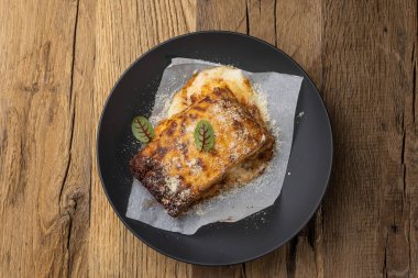 Tahta bir masada siyah tabakta bolonez lazanyası. Kapat.