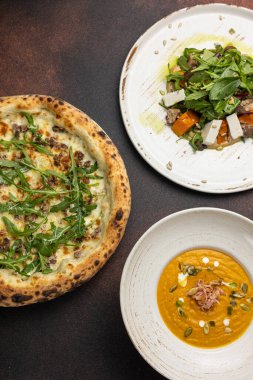 Lezzetli pizza, çorba ve salata masada.