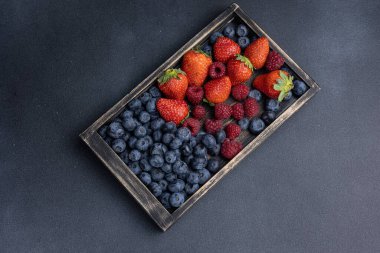 Yaban mersini, ahududu, çilek bir kutuda koyu bir arka planda.