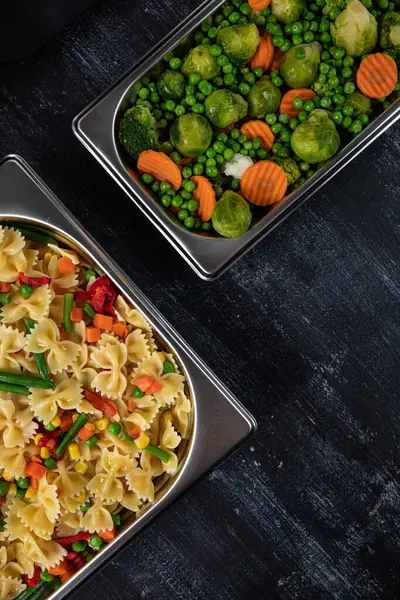 Containers with pasta and vegetables in the kitchen