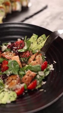 Karidesli salata, vişneli domates ve siyah tabakta avokado.