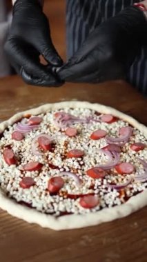 Şef sosisli, peynirli, domatesli pizza pişirir.