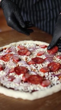 Şef sosisli, peynirli, domatesli pizza pişirir.