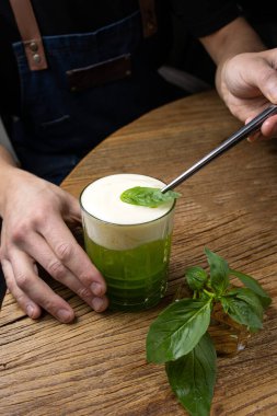 Tahta bir masada fesleğenli yeşil alkollü kokteyl..