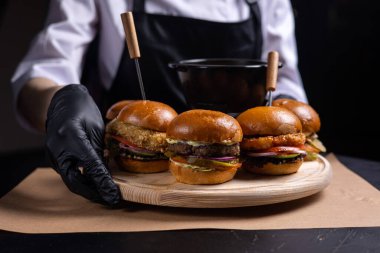 Hamburgerler ahşap bir tahtanın üzerinde bir şefin ellerinde.