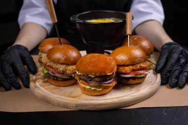 Hamburgerler ahşap bir tahtanın üzerinde bir şefin ellerinde.