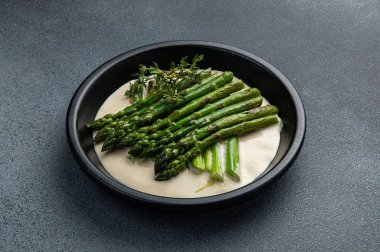 Siyah bir kasede siyah bir arka planda kremalı kuşkonmaz.