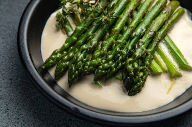 Siyah bir kasede siyah bir arka planda kremalı kuşkonmaz.