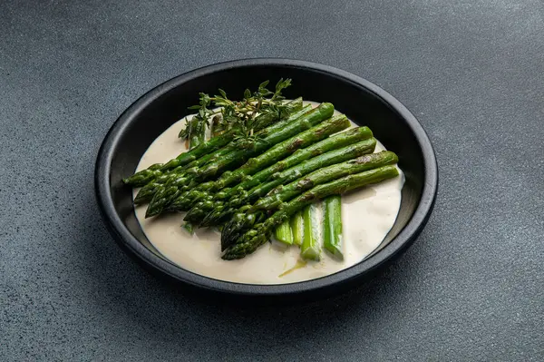 Siyah bir kasede siyah bir arka planda kremalı kuşkonmaz.