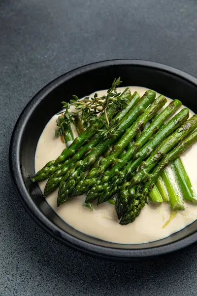 Siyah bir kasede siyah bir arka planda kremalı kuşkonmaz.