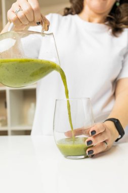 Bir kadın sürahiden yeşil bir meyve suyu bardağa dolduruyor.