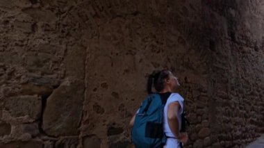 Castiglione della Pescaia İtalya, Haziran 05, 2023: Antik şehir duvarlarının yanında yürürken gülümseyen ve etrafa bakan bir turist