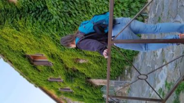 Bir turist kızın yokuş yukarı yürüdüğü ve arka planda sarmaşıkla kaplı bir evin olduğu dikey bir video.