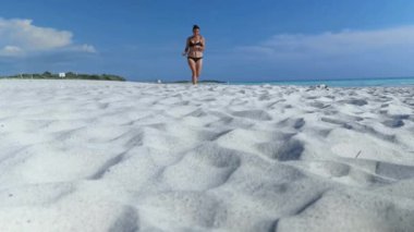 Güneşin altında beyaz bir plajda koşarken mayolu ve yalınayak bir kız.